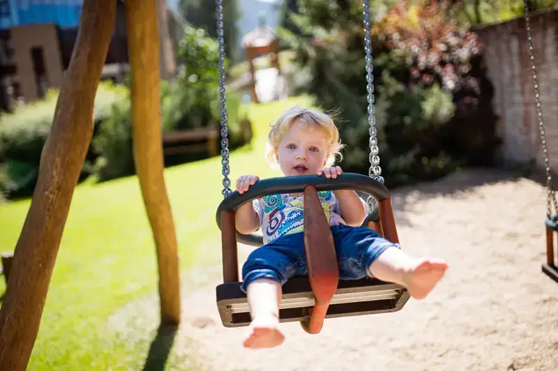 Kleinkind sitzt lachend in einer Babyschaukel auf dem Spielplatz